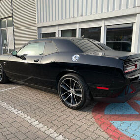 Schwarzer Dodge Challenger Sportwagen auf Parkplatz vor Autohausgebäude