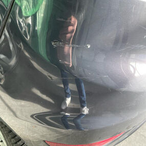 Kratzer und Lackschäden an der hinteren Stoßstange eines dunkelgrauen Autos im Tageslicht.