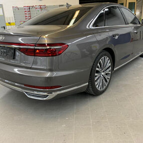 Grauer Audi A8 Limousine steht in heller Werkstatt, hochwertige Alufelgen und LED-Rückleuchten.
