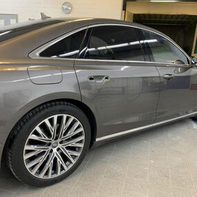 Grauer Audi Limousine mit Alufelgen steht in moderner Werkstatt für Autoreparatur.