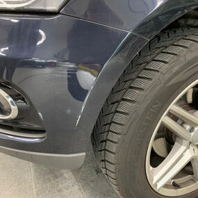 Kratzer am vorderen Kotflügel eines dunklen Autos mit Winterreifen und Alufelge.