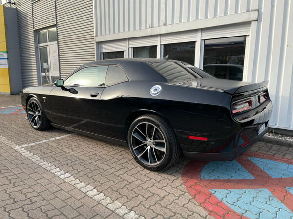 Schwarzer Dodge Challenger Sportwagen auf Parkplatz vor Autohausgebäude