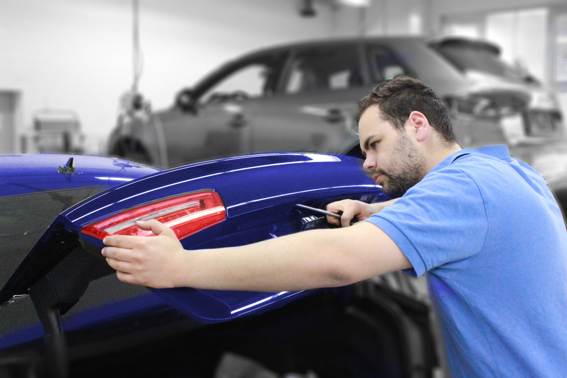 Kfz-Mechaniker montiert Rückleuchte am blauen Auto in der Werkstatt.